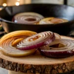 Thin slices of golden brown caramelized onions in a rustic kitchen setting, surrounded by fresh herbs.