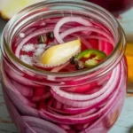 A beautifully styled jar filled with vibrant pickled red onions against a rustic wooden backdrop.