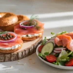 Bagels with cream cheese and smoked salmon beside a salad with avocado and cherry tomatoes.